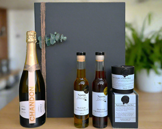 Bottles of Chandon champagne and Nivous olive oil and balsamic vinegar on a table with a gray backdrop.