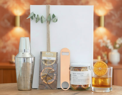 Decorative items including a cocktail shaker, card, and jar on a wooden surface with a neutral background.